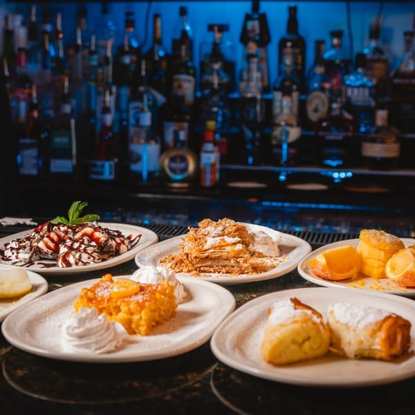 Assortment of desserts including baklava, cakes, and pastries on a bar with liquor bottles.