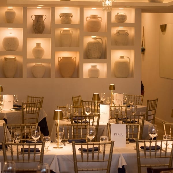 Elegant dining room at Perla restaurant with gold chairs, white tablecloths, and illuminated wall niches.