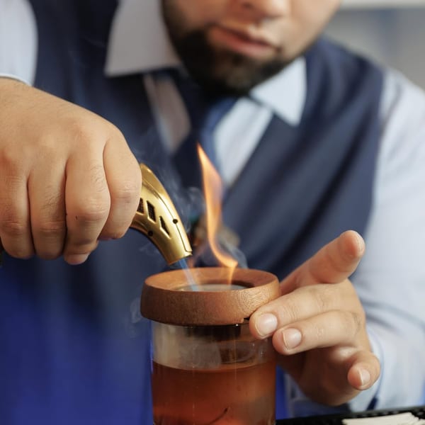 Bartender smoking a cocktail with a torch, creating a smoky, aromatic drink.