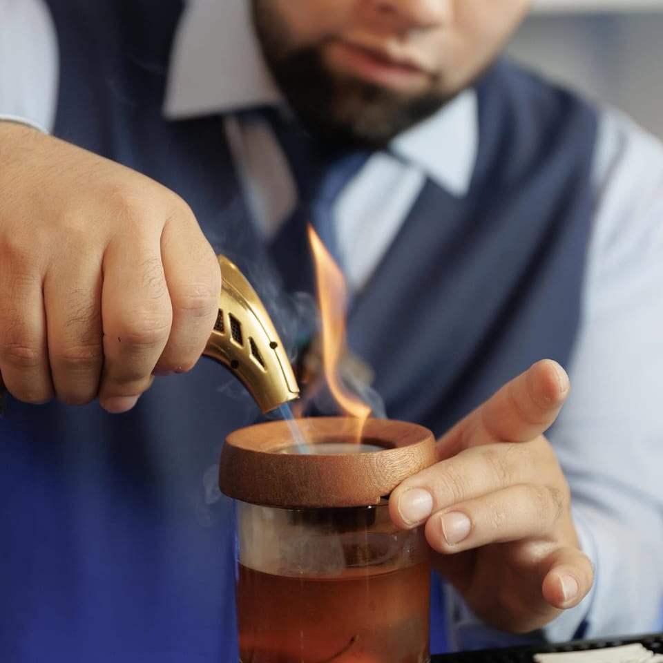 Bartender smoking a cocktail with a torch, creating a smoky, aromatic drink.
