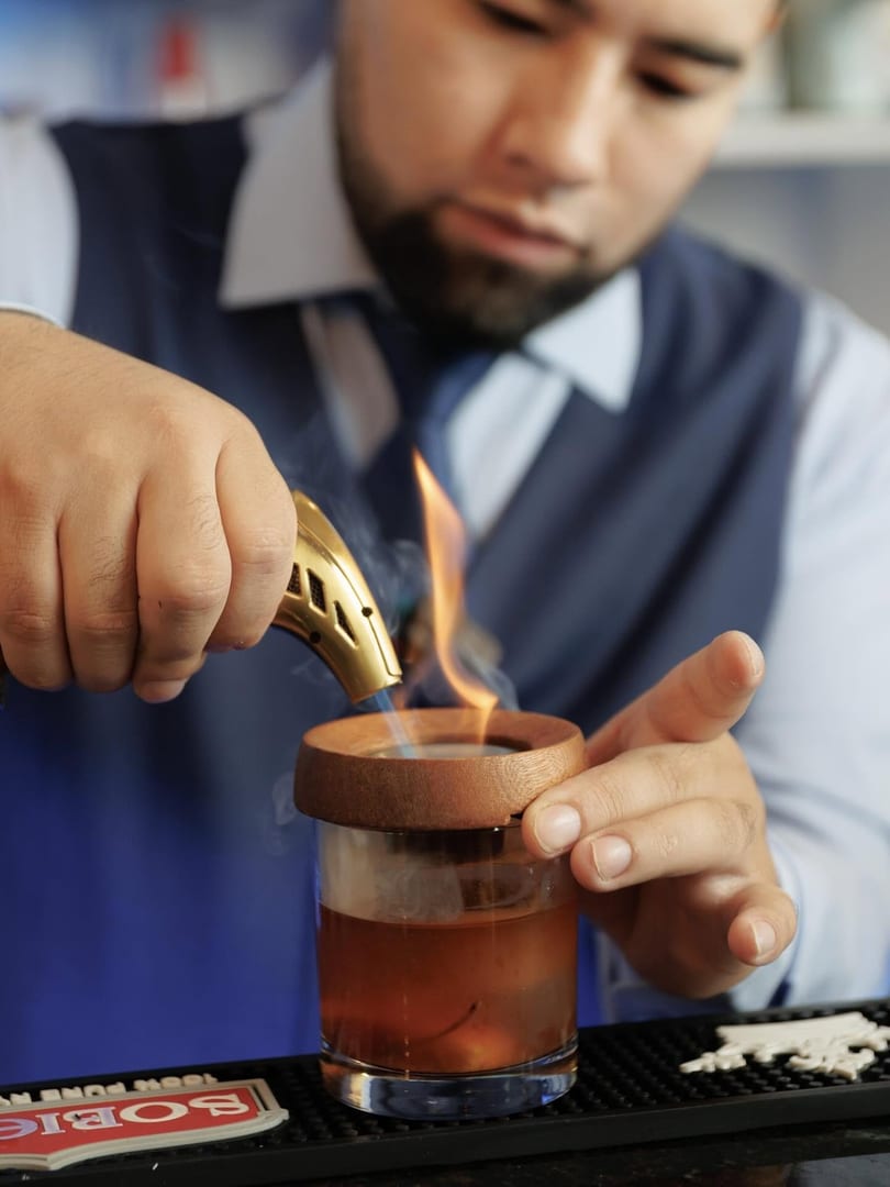 Bartender smoking a cocktail with a torch, creating a smoky, aromatic drink.