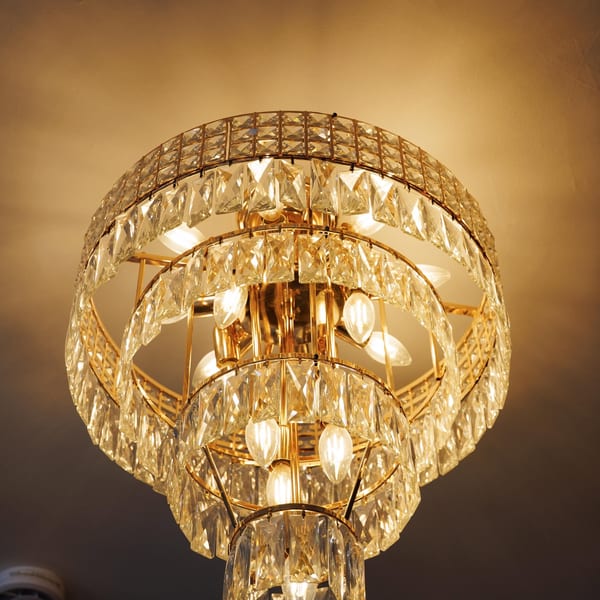 A luxurious, multi-tiered crystal chandelier with warm glowing bulbs hangs from a ceiling.