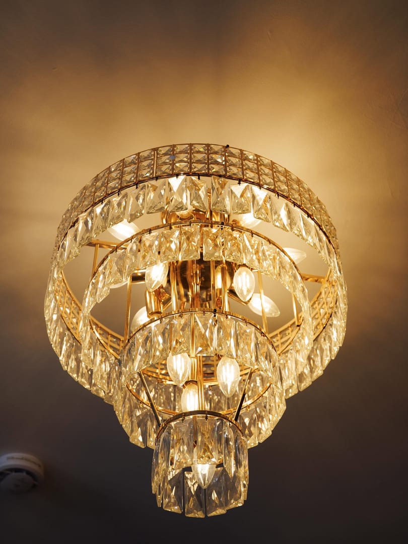 A luxurious, multi-tiered crystal chandelier with warm glowing bulbs hangs from a ceiling.
