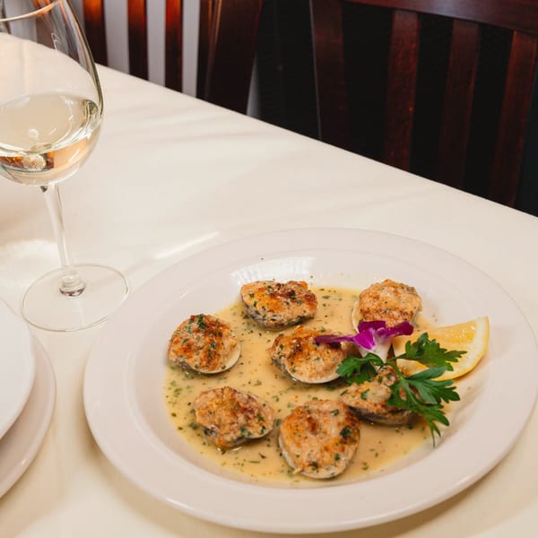 Baked clams in a creamy sauce with lemon and parsley, next to a glass of white wine.