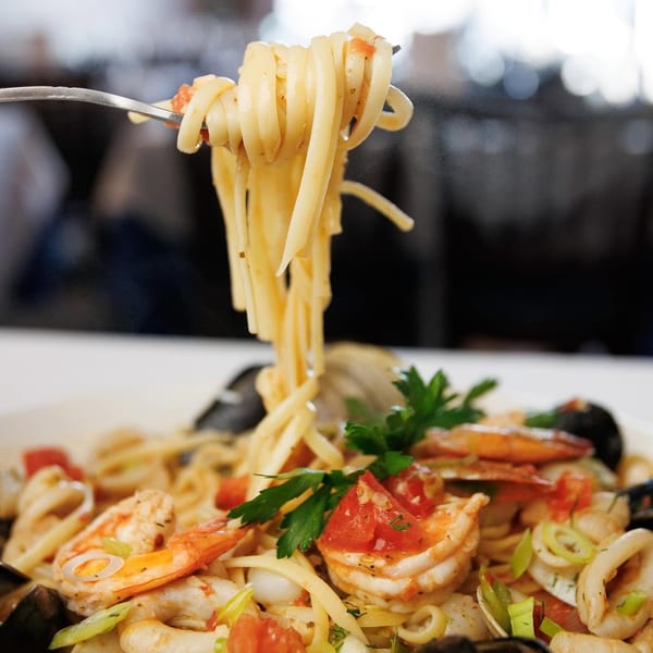 A fork lifts linguine pasta from a bowl of seafood pasta with shrimp, mussels, clams, and calamari.