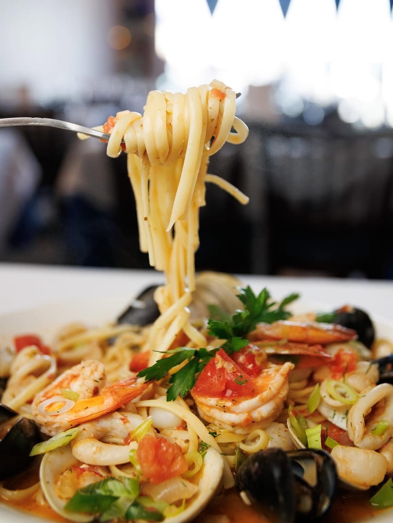 A fork lifts linguine pasta from a bowl of seafood pasta with shrimp, mussels, clams, and calamari.