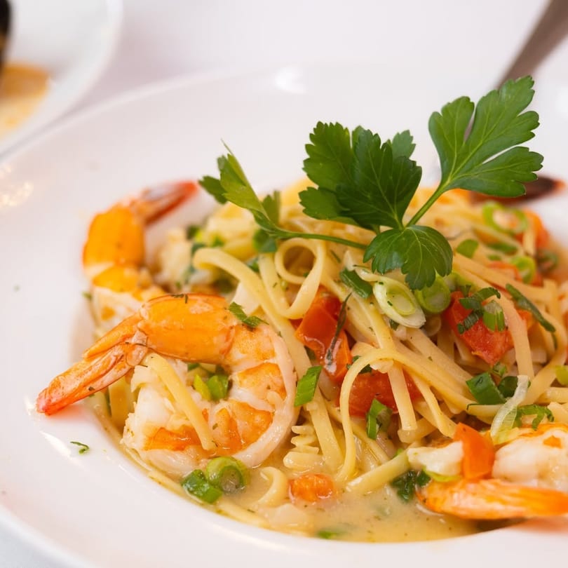 Close-up of shrimp scampi with linguine, tomatoes, and green onions, garnished with parsley.