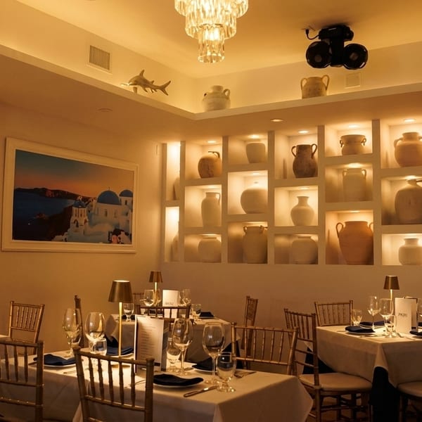 Warmly lit restaurant dining room with set tables, a large painting, and decorative pottery in wall niches.