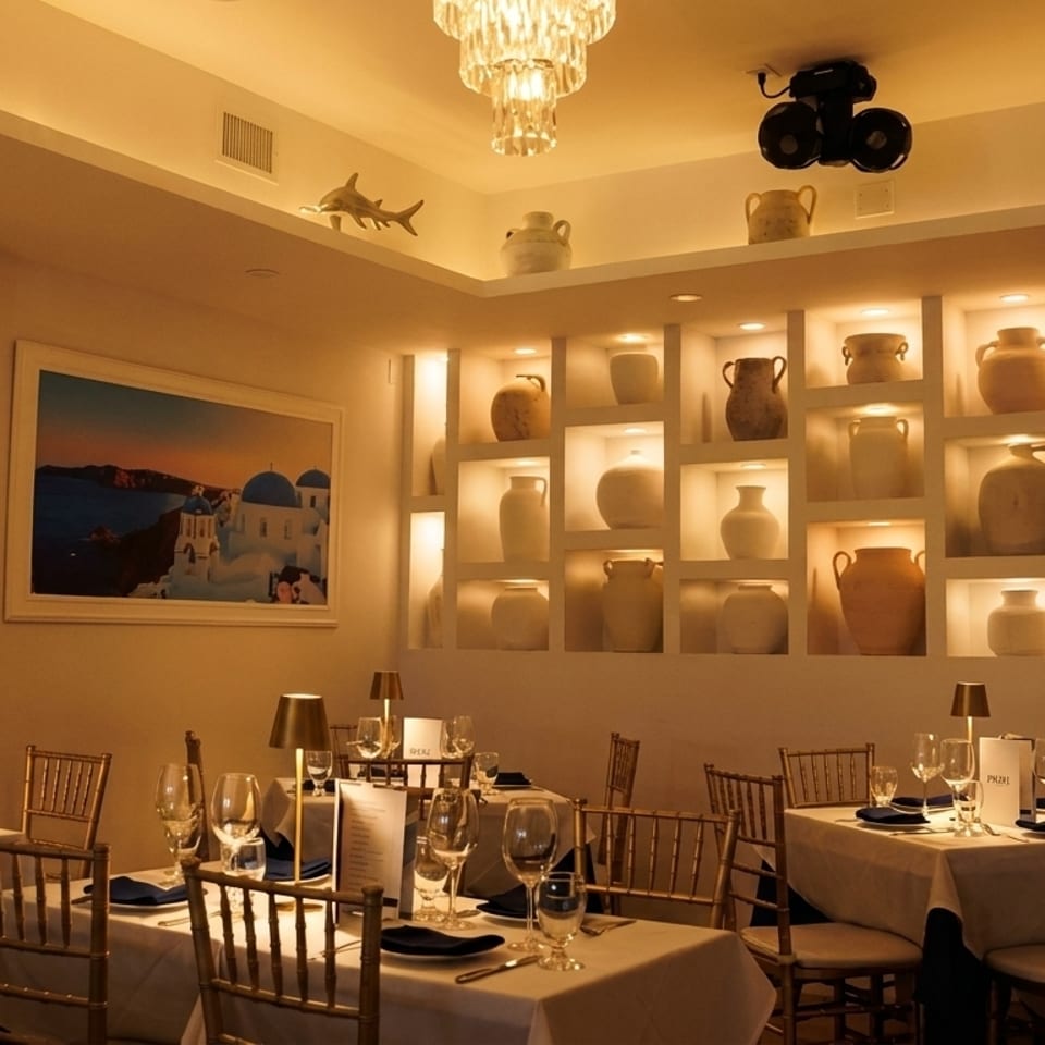 Warmly lit restaurant dining room with set tables, a large painting, and decorative pottery in wall niches.